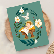 Christmas card with Baby Jesus in a manger surrounded by florals and holly, holding a sprig of holly in His hand.