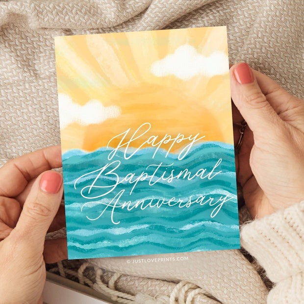 This image displays a beautifully designed card with the message "Happy Baptismal Anniversary" in elegant, flowing white script. The background showcases a bright, stylized sun rising over calm blue waves, creating a warm, inviting atmosphere. The soft yellow hues of the sun blend seamlessly with fluffy clouds, adding a serene and celebratory tone, ideal for commemorating this special anniversary.