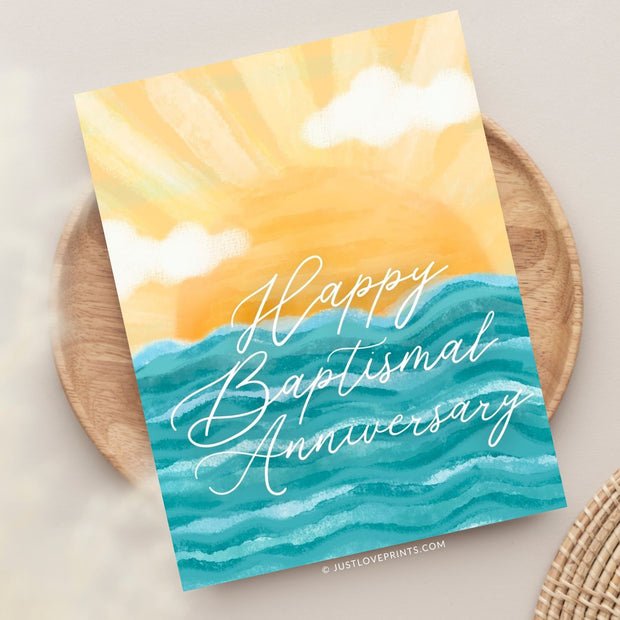 This image displays a beautifully designed card with the message "Happy Baptismal Anniversary" in elegant, flowing white script. The background showcases a bright, stylized sun rising over calm blue waves, creating a warm, inviting atmosphere. The soft yellow hues of the sun blend seamlessly with fluffy clouds, adding a serene and celebratory tone, ideal for commemorating a special anniversary.