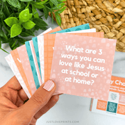 Hand holding a set of colorful cards with a question on one card, with plants and a woven basket in the background.