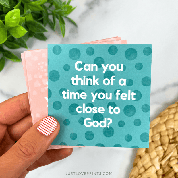 Hand holding a teal card with polka dots and text, with a plant and woven basket in the background.