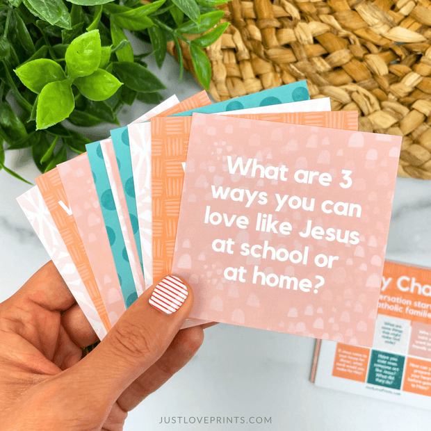 Hand holding a set of colorful cards with a question on one card, with plants and a woven basket in the background.