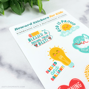 Sheet of colorful reward stickers for kids on a marble surface with green leaves.