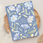 This card design features a heartfelt message, "Thank you for helping me grow in Faith," centered among delicate watercolor-style flowers. The background is a soft, muted blue, complementing the gentle tones of light blue and white flowers, which are accented with golden highlights on the petals and leaves. The botanical elements create a sense of grace and gratitude, making this design ideal for expressing appreciation with a spiritual touch.