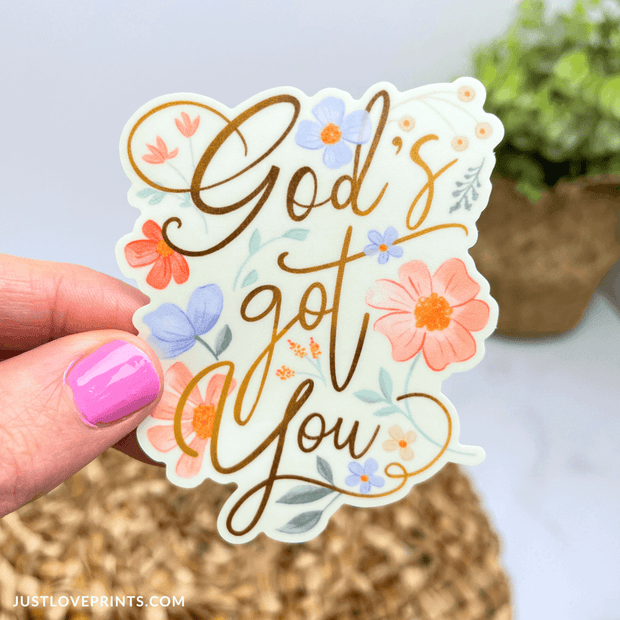 Floral sticker featuring the uplifting phrase "God's got you" in elegant script, surrounded by pastel flowers. A comforting reminder of faith and trust.