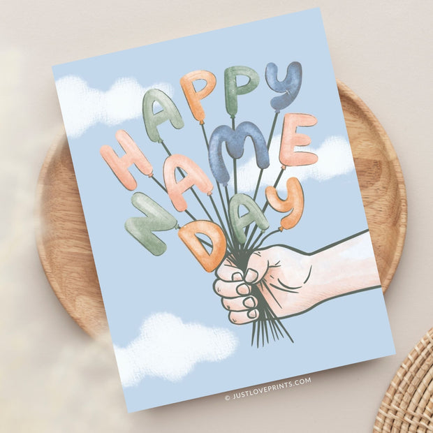 This card design celebrates a "Happy Name Day" with playful charm. It features a hand holding a bundle of balloon letters that spell out the greeting in cheerful pastel colors, including soft oranges, greens, and blues. The background is a light sky blue with soft white clouds, giving a whimsical, uplifting feel to the design. Perfect for marking a special Name Day with a joyful, personalized touch.