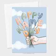 This card design celebrates a "Happy Name Day" with playful charm. It features a hand holding a bundle of balloon letters that spell out the greeting in cheerful pastel colors, including soft oranges, greens, and blues. The background is a light sky blue with soft white clouds, giving a whimsical, uplifting feel to the design. Perfect for marking a special Name Day with a joyful, personalized touch.