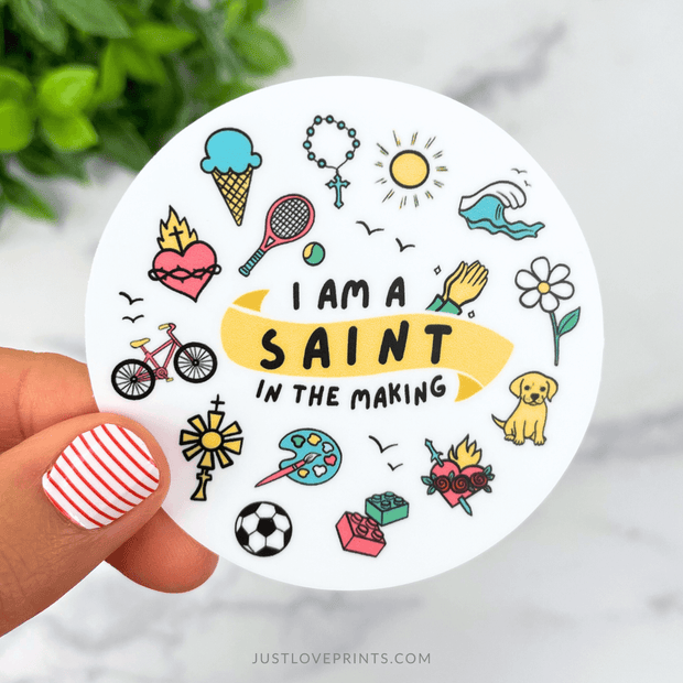 Colorful vinyl sticker with doodles of flowers, bike, ice cream, and sports items surrounding the phrase “I am a Saint in the Making.”