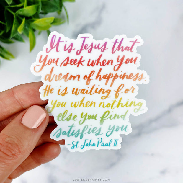 This sticker displays St. John Paul II's quote, "It is Jesus that you seek when you dream of happiness." The text flows in a warm gradient from pink to green, creating a peaceful, encouraging design.