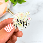 Hand holding a floral keychain with 'JMJ' text on a light background