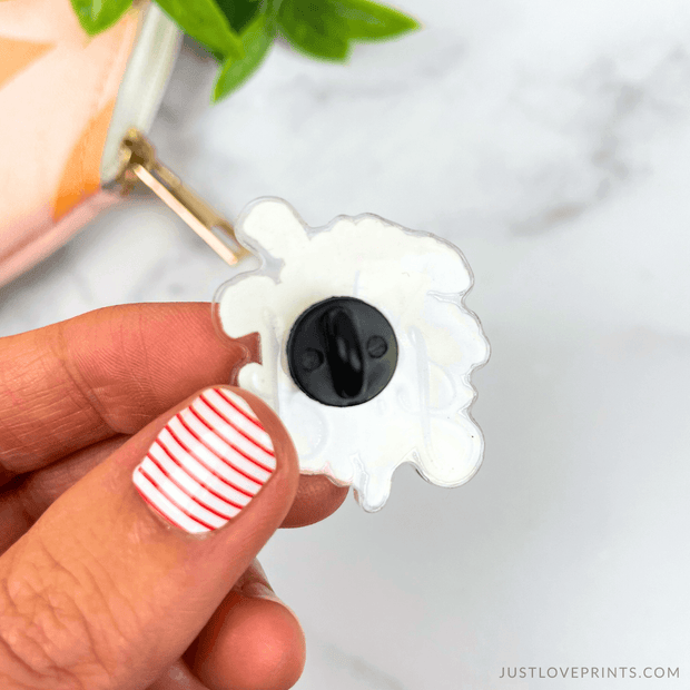White pin with black pin backing held by a hand. 