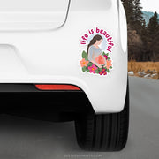 Sticker on a car bumper with 'life is beautiful' text and floral design, outdoors.
