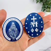 Two dark blue stickers, one with front of Miraculous Medal and the other of the back. 