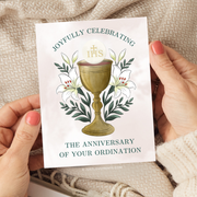 Card with a chalice illustration and text held by hands against a textured fabric background