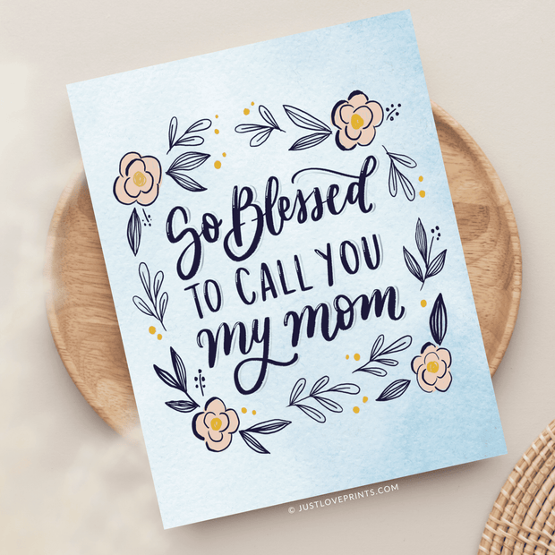 A greeting card with elegant script reading "so blessed to call you my mom" surrounded by a floral design with yellow and pink flowers and navy leaves,