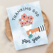 An illustrated card with the text "thanking god for you" features a hand holding a bouquet of colorful flowers and a rosary, set against a light blue background with a watercolor effect.