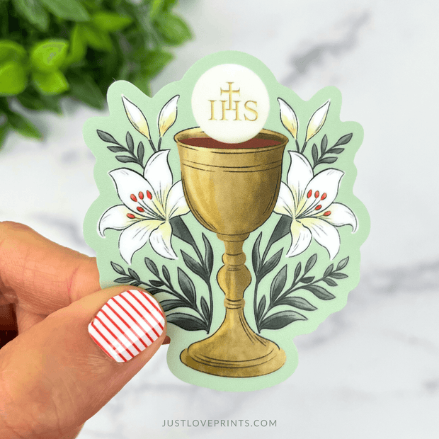 Sticker with golden chalice, Eucharist host with IHS letters, and white lilies around it.
