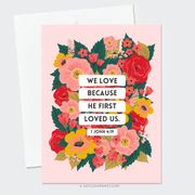 Floral pink greeting card featuring the Bible verse:
"We love because He first loved us." – 1 John 4:19.