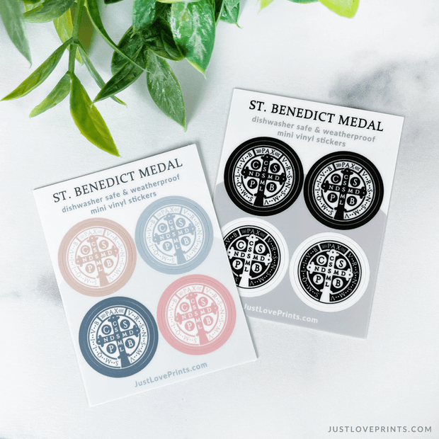These sticker sheets contain 4 St Benedict medal stickers. One sheet has colored medals, with tan, blue, navy, and pink. The other sheet is black and white. 