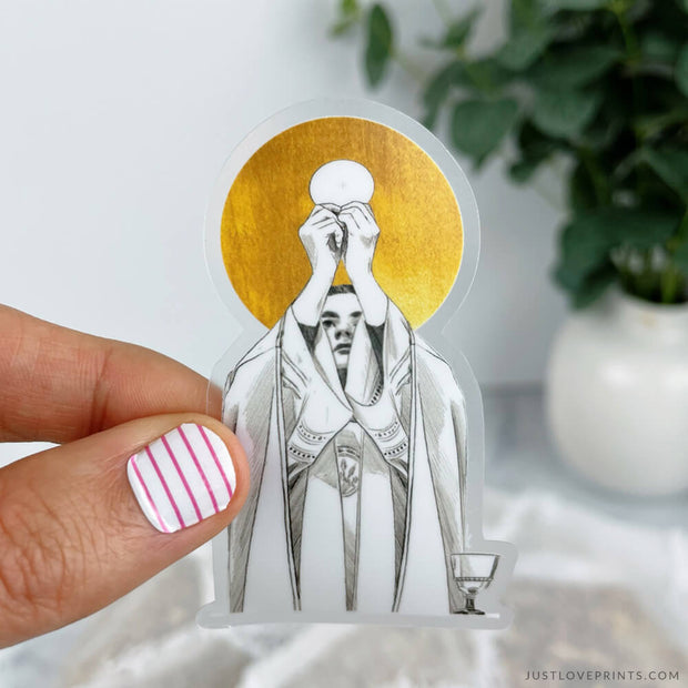 This sticker displays a priest dressed in his garments raising the Eucharist with a chalice to his left. There is a golden halo behind his head. 